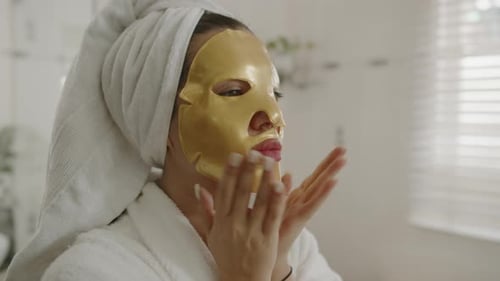 Woman Smoothing Golden Mask on Face