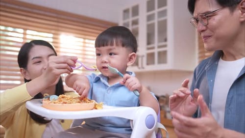 Happy Family Feeding Toddler Spaghetti in Kitchen