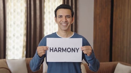 Smiling Man Holding "Harmony" Sign Indoors