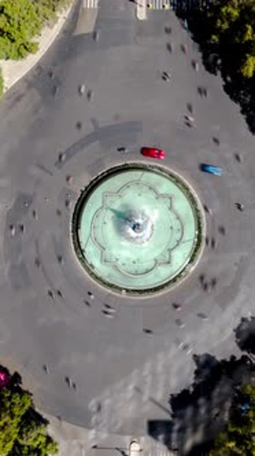 Aerial hyperlapse drone rotating over Fuente de la Diana Cazadora with motion blur traffic on Paseo