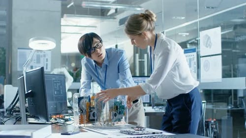 Two Computer Engineers Choose Printed Circuit Boards to Work with. In The Background Technologicall