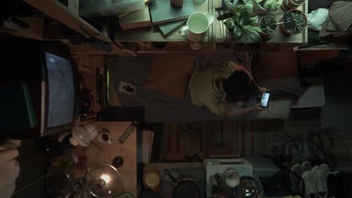 Top View of Asian Shoebox Flat Dweller Playing Game on Smartphone