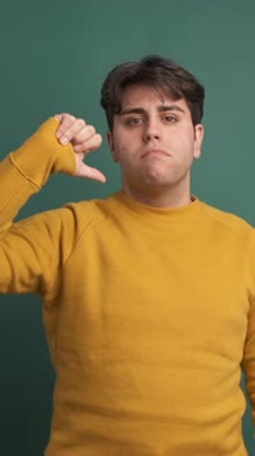 Upset Young Man Gesturing Thumb Down in Green Studio