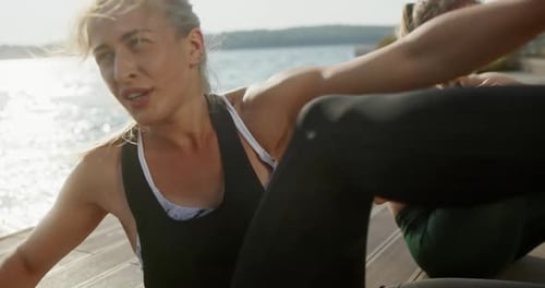 Two Fit Woman Working Out on a Deck on a Lake Shore in Evening Light with a Reflection Across the