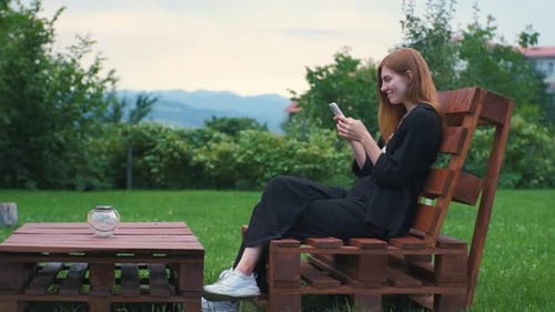 Beautiful Young Woman Enjoying the Sunset in Her Garden and Communicating on the Internet on a