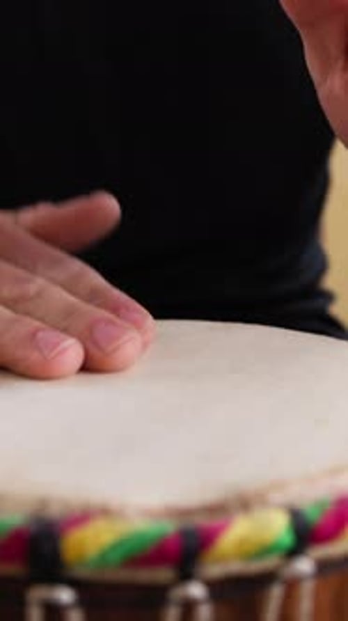 Hände eines Musikers, der eine Trommel zwischen seinen Beinen spielt