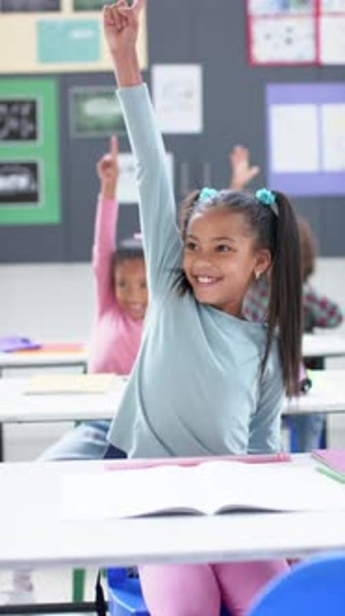 Vertical video: In school, girl raising hand in classroom, actively participating in lesson