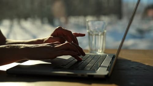 Nahaufnahme der Hände einer nicht erkennbaren Freelancerin, die auf einem Laptop tippt und am Schreibtisch sitzt, auf dem Hintergrund von