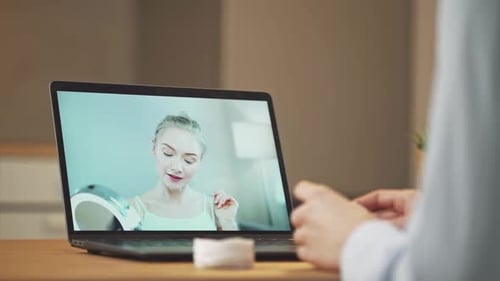 Una joven aprende a maquillarse mientras ve la lección de una bloguera de belleza en una computadora portátil