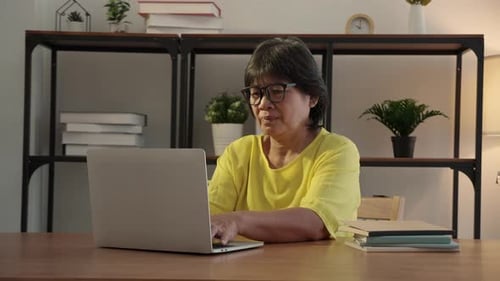 Elderly woman using laptop with office desk at home, senior woman typing on laptop.