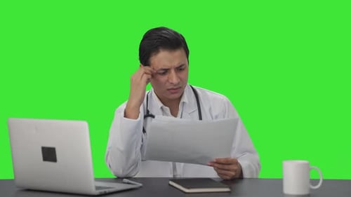 Stressed and tensed Indian doctor checking medical reports Green screen