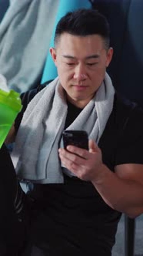 A Focused Man Dressed in Gym Attire is Actively Using His Smartphone in a Gymnasium