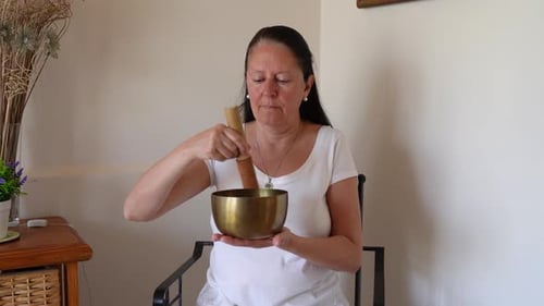 A Woman Striking A Tibetan Bowl With A Wooden Mallet For Sound Therapy. Close-up Shot