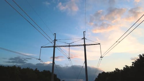 Dark Silhouette of High Voltage Tower with Electric Power Lines at Sunset