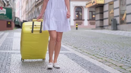 Woman Pulling Yellow Suitcase on Cobblestone Street