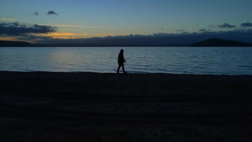 Einsamer Mann, der bei Sonnenuntergang langsam alleine an der Küste entlang geht, mit Horizont im Hintergrund