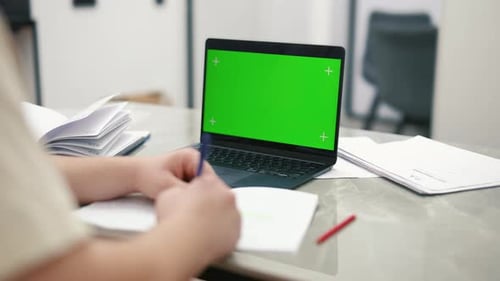 Student taking notes using a laptop with green screen