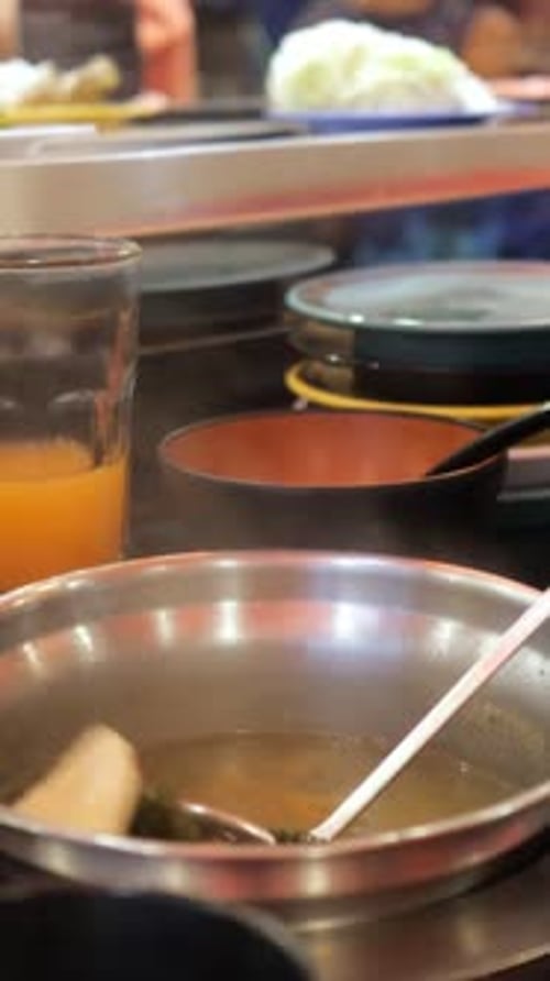 Cuchara con cucharón mariscos y verduras del caldo de acero inoxidable en el mostrador de un concurrido restaurante al vapor