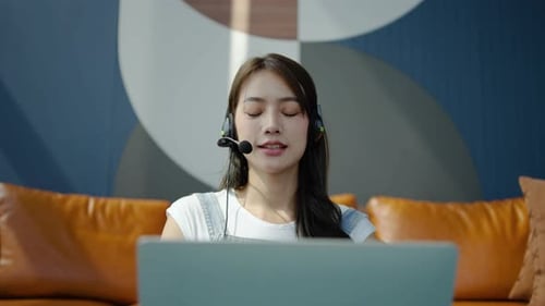 Consultant girl wearing headset with microphone sitting on sofa, freelance worker, call center