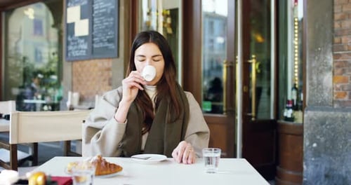One morning a beautiful elegant woman eats breakfast at the outdoor bar with a coffee and croissan