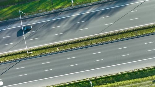 Drone shot of multiple cars traveling on wide multi‑lane highway divided by grassy median under