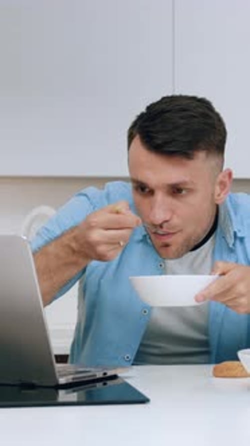 Man Eating Breakfast and Using Laptop at Kitchen