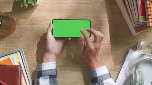 Ansicht der Hände eines Mannes von oben nach unten mit einem Greenscreen-Smartphone auf einem Holzschreibtisch