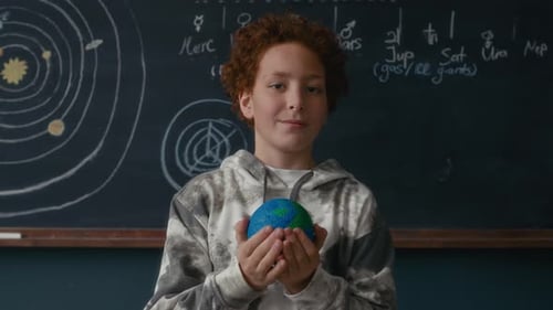 Portrait of Student Holding Earth Model in Front of Solar System Chalkboard