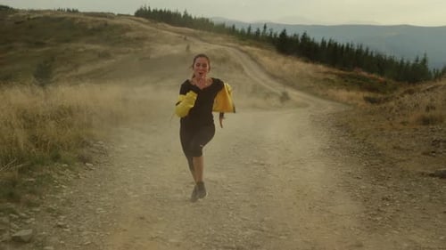 Smiling young sportswoman training fast on dirty road in beautiful mountains landscape