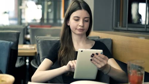 Teenage Girl Surfing Internet On Tablet Sitting In Cafe