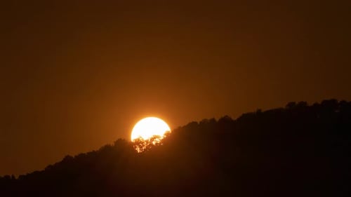 Golden Sunset Behind a Tree-Covered Hill