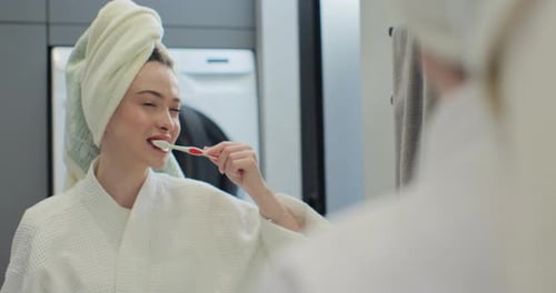 Woman Brushing Teeth in Bathroom Mirror