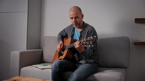 Man Plays Acoustic Guitar on Couch Indoors