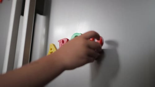 Close-up: Child's hand places magnet alphabet letter on kitchen fridge