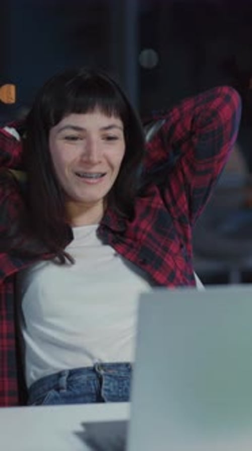 Young Happy Caucasian Woman Sitting in Dark Office Finishing Work Looking on Laptop Monitor