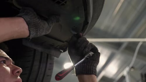 An Auto Mechanic Working Under the Car on a Car Lift in the Garage Car Service