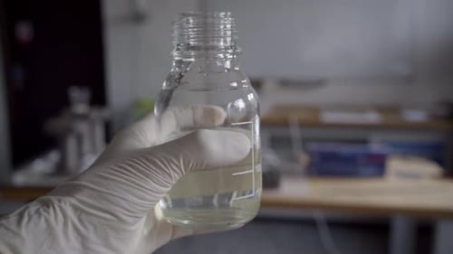 Main avec des gants de laboratoire tenant un bécher, Ralentissement