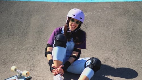 Skateboarder Sits on Ground at Skatepark