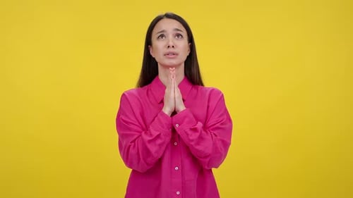 Woman Prays with Crossed Fingers Against Yellow Background