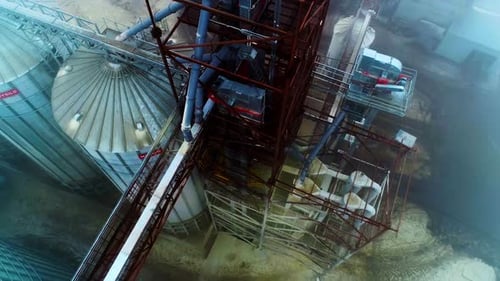 High construction towering over the granary elevator tanks. Flying over the silo complex.