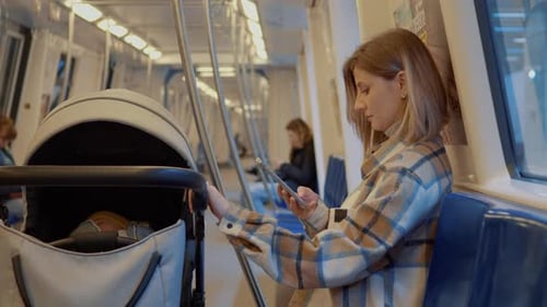 Young mother using smartphone while traveling on subway with baby stroller