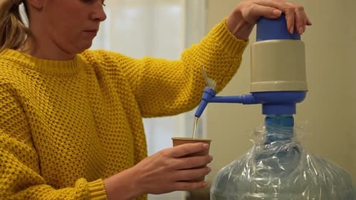 Person Filling Cup with Water From Large Dispenser