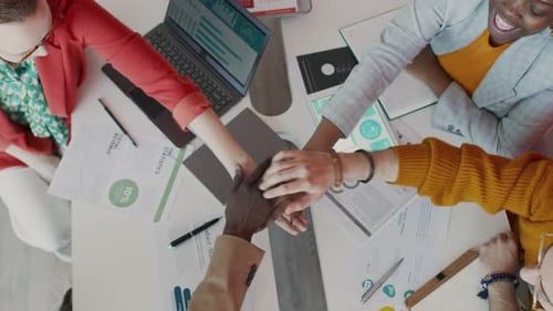 Top View of Diverse Creative Team Linking Hands in Middle at Project Meeting