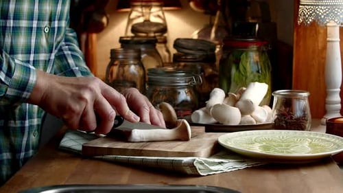 Man Cuts Mushrooms on Wooden Board in Kitchen