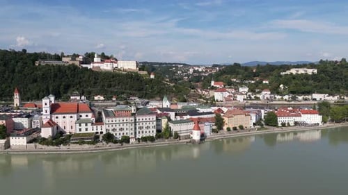 Aerial view of a historic city's buildings with red-tiled roofs lining the riverbank, shadowed by a