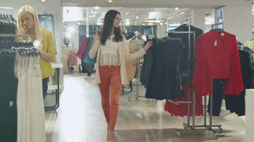 Happy young brunette girl is walking though a clothing store in orange trousers.