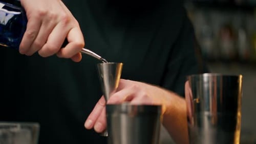 Closeup a Male Bartender Hands Holding Bottle and Masterfully Pours Liquor Into Steel Jigger