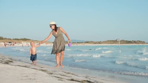 Cheerful mother and son walking along sandy beach on summer vacation