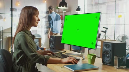 Beautiful Brunette Female Video Editor Works on Her Personal Computer with Big Green Screen Mock Up