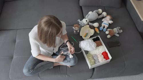 Woman Crafts Yarn Dolls on Gray Couch